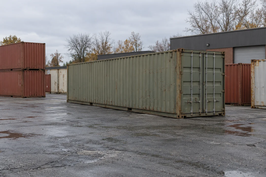 Illustrative image of shipping containers in a paved yard with industrial buildings and autumn trees behind